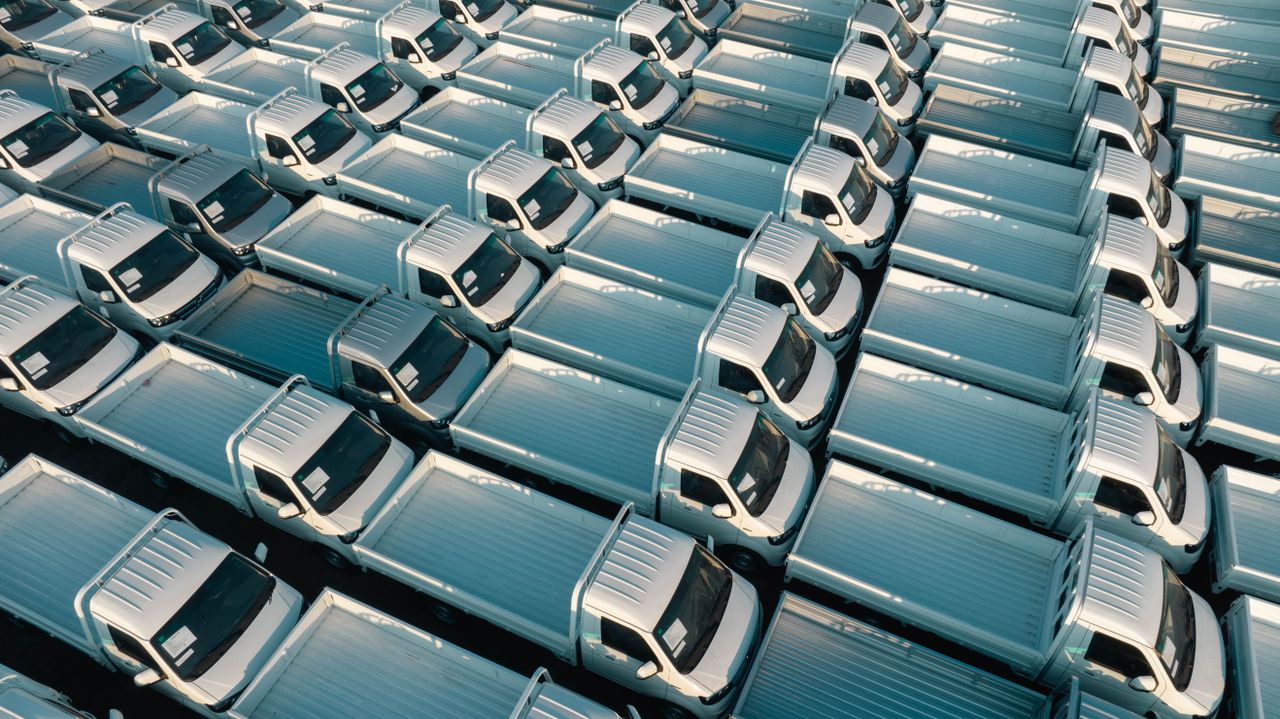 A top-down view of numerous white trucks parked in a grid pattern, showing symmetry and industrial logistics.